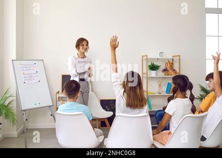 Gruppo di studenti delle scuole elementari che si alzano le mani per rispondere alla domanda in aula Foto Stock