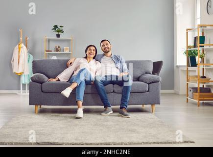 Una giovane coppia sorridente e felice si siede insieme su un comodo divano a casa nel soggiorno, guardando la macchina fotografica. Senso di armonia nelle relazioni Foto Stock