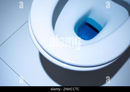 Vista ravvicinata all'interno del recipiente del water. Bagno rifinito con piastrelle bianche e cotto bianco. Foto Stock