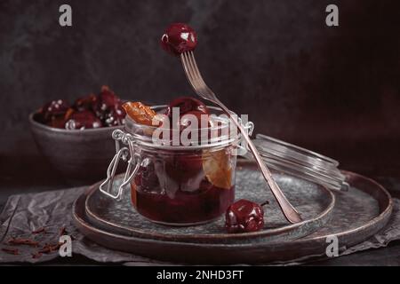 Prugne marinate con spezie in vaso di vetro sul tavolo da cucina Foto Stock