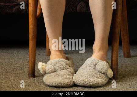 piedi femminili in pantofole grigie sul tappeto nella camera da letto, piedi in pantofole, comfort di casa Foto Stock