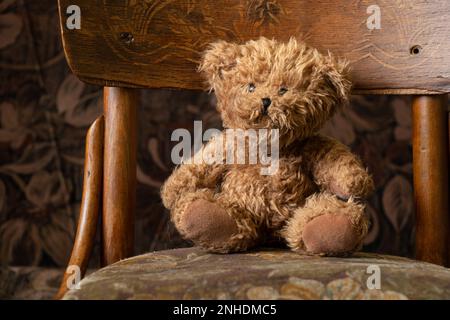 l'orso bruno di peluche siede su una vecchia sedia a casa, il giocattolo dei bambini Foto Stock