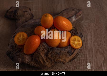 Primo piano di piccole arance cinesi (Citrus sinensis) o Kumquat su una radice di un albero su una tavola di legno Foto Stock