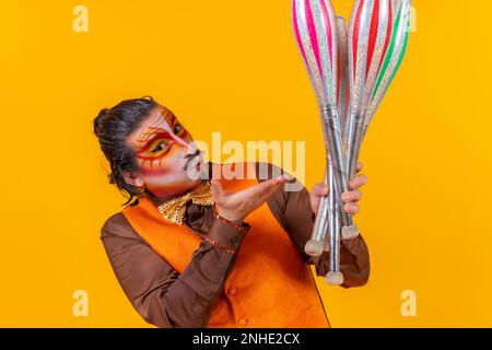 Bacio e ritratto di felice giocoliere uomo in giubbotto di trucco giocolieri su sfondo giallo Foto Stock