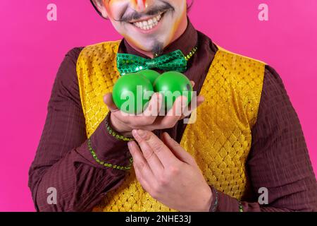 Ritratto di clown con trucco facciale bianco su sfondo rosa, giocolando palle verdi Foto Stock