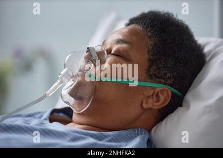 Vista laterale primo piano di una donna anziana nera che dorme sul letto nella stanza dell'ospedale con maschera di supporto dell'ossigeno Foto Stock