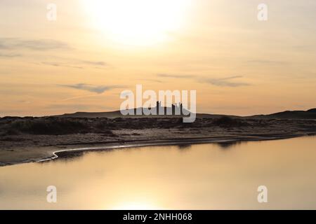 Dunstanburgh Castle all'alba attraverso Embleton Bay, Northumberland Foto Stock