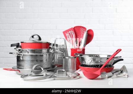 Set di utensili da cucina puliti su tavolo bianco contro muro di mattoni Foto Stock