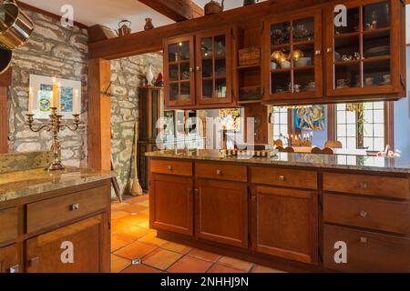 Armadietti in legno tinto stile shaker e piani in granito sfumato in cucina con pavimento in piastrelle di ceramica terracotta all'interno della vecchia casa circa 1830. Foto Stock