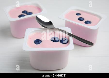 Tazze di plastica con gustosi yogurt e mirtilli su un tavolo di legno bianco Foto Stock