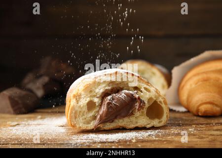 Cospargere lo zucchero in polvere su un gustoso croissant con cioccolato su un tavolo di legno Foto Stock
