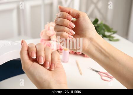 Donna che fa manicure con lampada ultravioletta delle unghie a tavolo bianco, primo piano Foto Stock