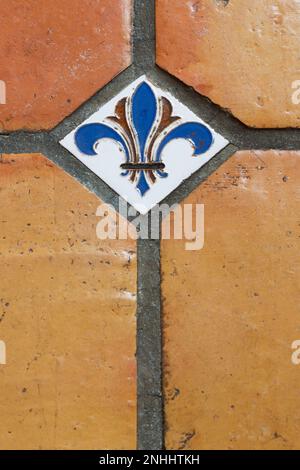 Piccola ceramica decorativa simbolo Fleur-de-lys mattonelle in ceramica tra quattro più grandi piastrelle in terracotta ceramica pavimento in sala da pranzo all'interno della vecchia casa. Foto Stock