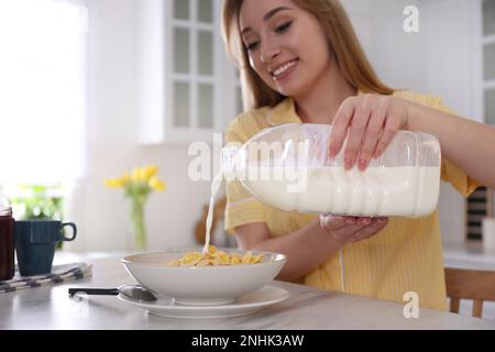 Giovane donna che versa latte da una bottiglia di gallone nel piatto con cereali per la colazione al tavolo di marmo bianco in cucina Foto Stock