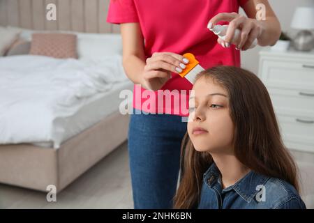Madre usando nit pettine e spray sui capelli della figlia a casa. Trattamento antighiaccio Foto Stock