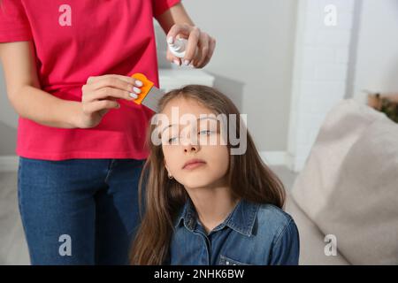 Madre usando nit pettine e spray sui capelli della figlia a casa. Trattamento antighiaccio Foto Stock