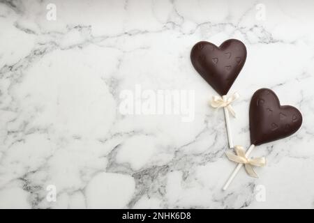 Lollipop a forma di cuore al cioccolato su tavolo in marmo bianco, piatto. Spazio per il testo Foto Stock