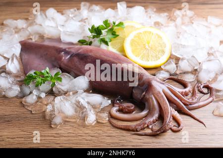 Calamari freschi crudi con ghiaccio, limone e prezzemolo sul tavolo di legno Foto Stock