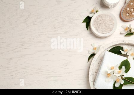 Piatto posa composizione con sale marino e bellissimi fiori di gelsomino su tavola di legno bianco, spazio per il testo Foto Stock