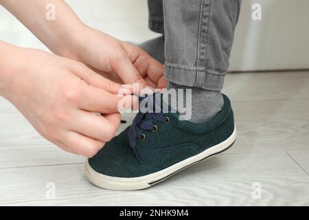 Madre che aiuta il figlio a legare i lacci delle scarpe a casa, primo piano Foto Stock