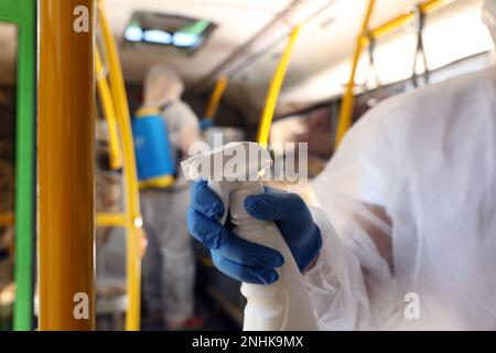 Servizi igienico-sanitari per i trasporti pubblici. Lavoratore in tuta protettiva disinfettare salone di autobus, primo piano Foto Stock