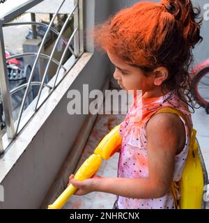 Dolce bambina indiana giocare i colori sul festival Holi, tenendo pichakaree piena di colori, festa Holi celebrazioni a Delhi, India Foto Stock