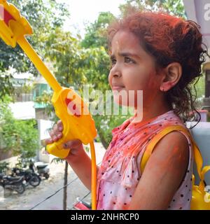 Dolce bambina indiana giocare i colori sul festival Holi, tenendo pichakaree piena di colori, festa Holi celebrazioni a Delhi, India Foto Stock