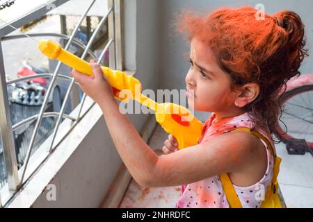 Dolce bambina indiana giocare i colori sul festival Holi, tenendo pichakaree piena di colori, festa Holi celebrazioni a Delhi, India Foto Stock