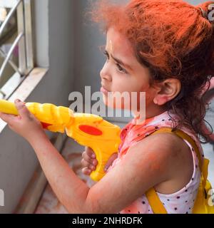 Dolce bambina indiana giocare i colori sul festival Holi, tenendo pichakaree piena di colori, festa Holi celebrazioni a Delhi, India Foto Stock