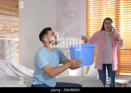 Giovane uomo che raccoglie l'acqua che perde dal soffitto mentre la sua ragazza che chiama il servizio di riparazione del tetto a casa Foto Stock