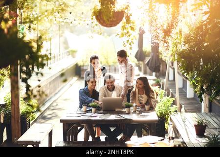 Un altro esempio di come la tecnologia riunisca le persone. un team di colleghi che utilizza un computer portatile insieme durante una riunione in un bar all'aperto. Foto Stock