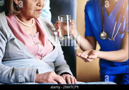 Questi vi faranno sentire meglio. un'infermiera che dà un farmaco e un bicchiere d'acqua ad un paziente. Foto Stock