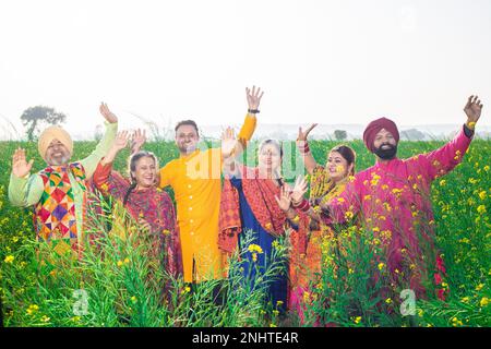 La famiglia Punjabi sikh che fa la danza del bhangra nel campo agricolo festeggia il festival di Baisakhi o vaisakhi. Foto Stock