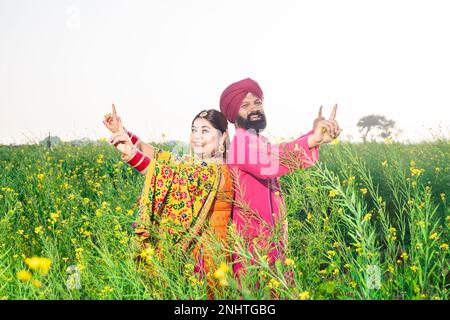 Happy Punjabi sikh coppia facendo bhangra danza in campo agricolo celebrare Baisakhi o vaisakhi festival. Foto Stock