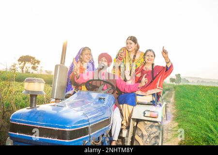 Felice famiglia contadina punjab seduta sul trattore ballando e festeggiando all'aperto. India rurale e concetto di prosperità. Foto Stock