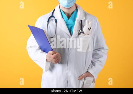 Pediatra con coniglio giocattolo e stetoscopio su sfondo giallo, primo piano Foto Stock