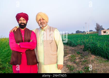 Ritratto di felice padre e figlio punjabi che indossano kurta e pagdi turbano in piedi insieme in campo agricolo. Foto Stock