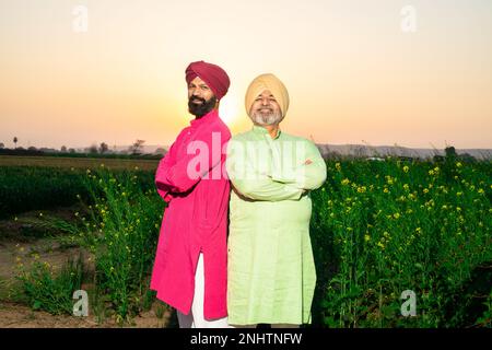 Ritratto di felici contadini dello srdar punjabi che indossano kurta e pagdi turbano in piedi insieme braccio trasversale al campo agricolo. Guardando la fotocamera. Foto Stock