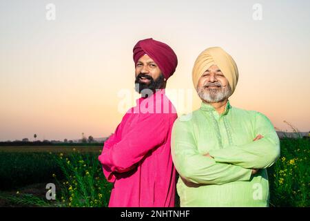 Ritratto di felici contadini dello srdar punjabi che indossano kurta e pagdi turbano in piedi insieme braccio trasversale al campo agricolo. Primo piano. Padre e figlio. Foto Stock