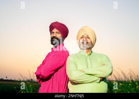 Ritratto di felici contadini dello srdar punjabi che indossano kurta e pagdi turbano in piedi insieme braccio trasversale al campo agricolo. Primo piano. Padre e figlio. Foto Stock