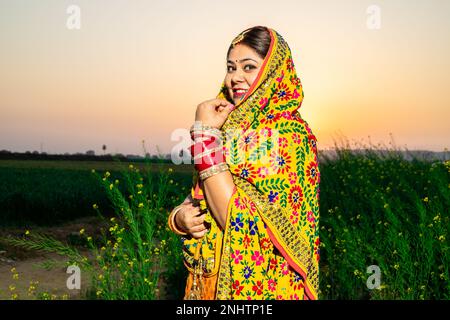 Ritratto di bella giovane indiana punjabi donna indossare colorato tradizionale in piedi al campo agricolo all'aperto. Foto Stock