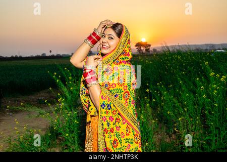 Ritratto di bella giovane indiano punjabi modello donna indossando colorato tradizionale in piedi posa in campo agricolo all'aperto. Foto Stock