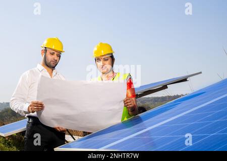 Giovane uomo indiano e tecnici donna in piedi e la pianificazione di installare pannelli solari. Lavoratori industriali discutere su impianto solare, alt Foto Stock