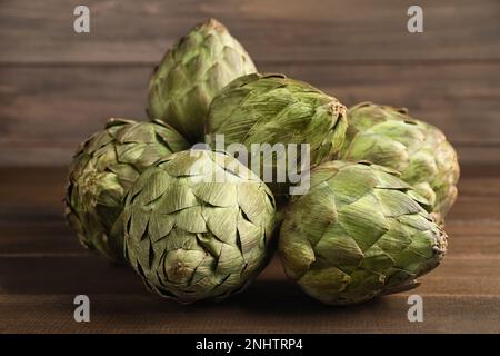 Molti carciofi freschi crudi su tavola di legno Foto Stock