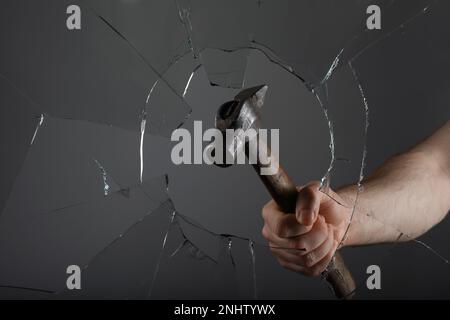 Uomo che rompe la finestra con martello su sfondo grigio, primo piano Foto Stock