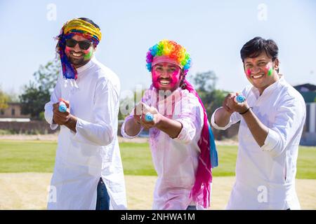 Allegri giovani amici maschi indiani che indossano un vestito di kurta bianca giocando con pichkari celebrando il festival holi all'aperto nel parco. Foto Stock
