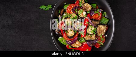 Melanzane alla griglia, peperone, zucchine, cipolla rossa, pomodoro con aglio su un piatto nero. Vista dall'alto, banner Foto Stock