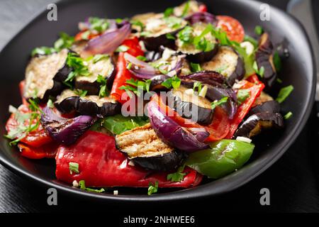 Melanzane alla griglia, peperone, zucchine, cipolla rossa, pomodoro con aglio su un piatto nero. Foto Stock