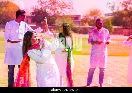 Felici giovani indiani indossando un vestito di kurta bianca che festeggia il festival di holi con polvere colorata o gulal al parco all'aperto. Foto Stock