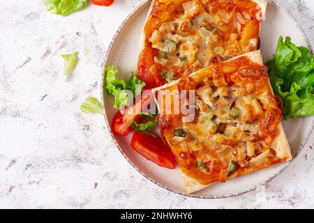 Mini pizza per bambini, piccole torte aperte con prosciutto, salsa di pomodoro, mozzarella e formaggio in cestino su sfondo chiaro. Vista dall'alto Foto Stock